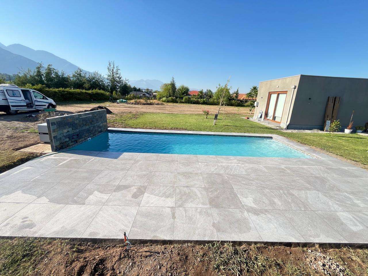 Piscina de fibra Ciprés terminada, con borde de porcelanato gris y cascada