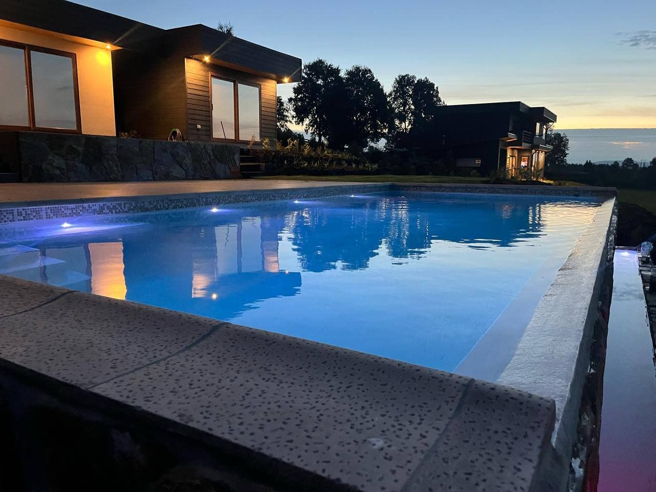 Piscina iluminada de noche con borde de piedra